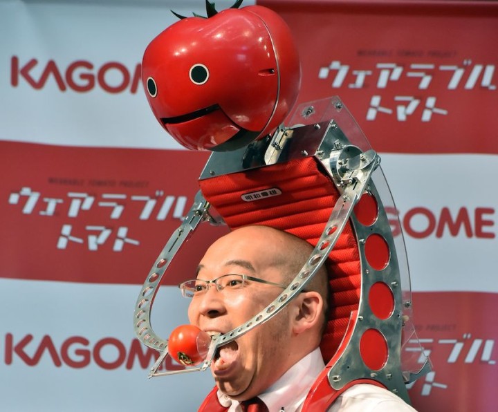 Japan's food company Kagome employee Shigenori Suzuki tries to eat a tomato which is provided from the newly developed tomato dispenser for marathon runner "Tomachan" during a demonstration ahead of this weekend's Tokyo marathon in Tokyo on February 19, 2015. The hands free tomato eating machine was developed by Japanese artist Nobumichi Tosa and Tosa also developed a compact one "Mini-Tomachan".     AFP PHOTO / Yoshikazu TSUNO